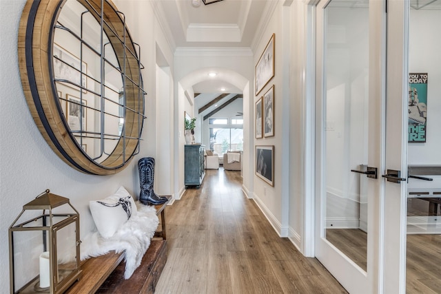 hall with baseboards, wood finished floors, crown molding, and arched walkways