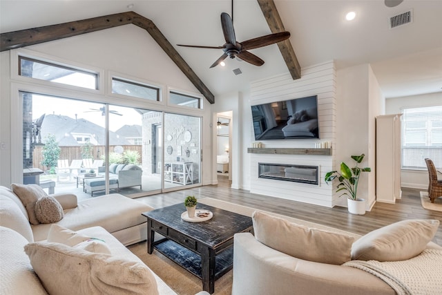 living area with a large fireplace, visible vents, wood finished floors, a ceiling fan, and beam ceiling