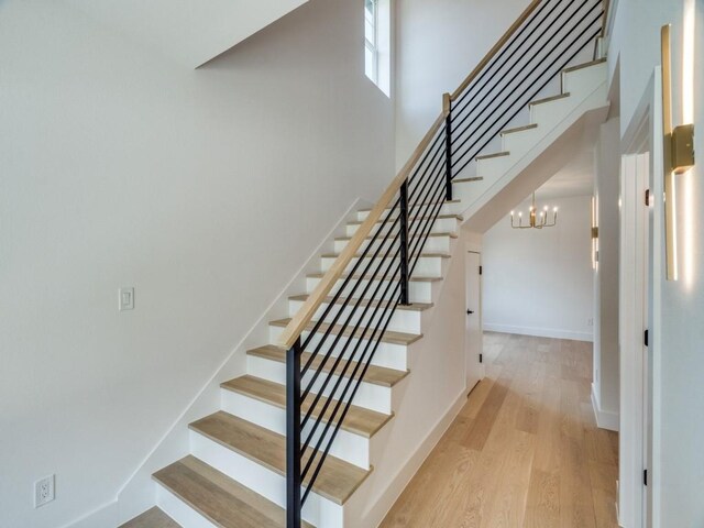stairway with a towering ceiling, a notable chandelier, baseboards, and wood finished floors