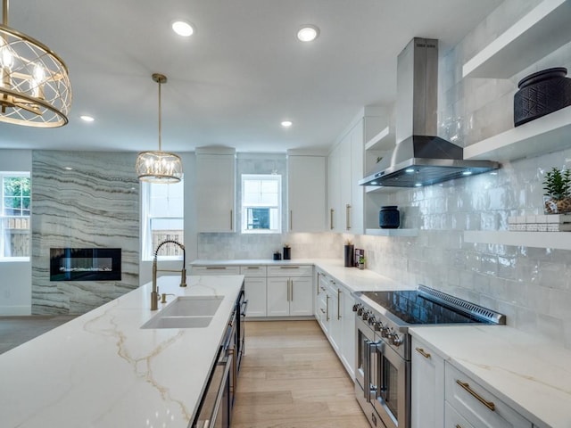 kitchen featuring a notable chandelier, range with two ovens, a sink, open shelves, and wall chimney range hood