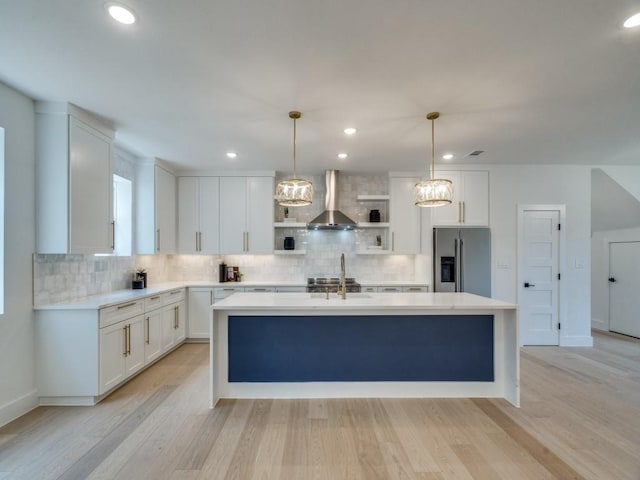 kitchen with white cabinets, an island with sink, open shelves, stainless steel fridge with ice dispenser, and wall chimney range hood