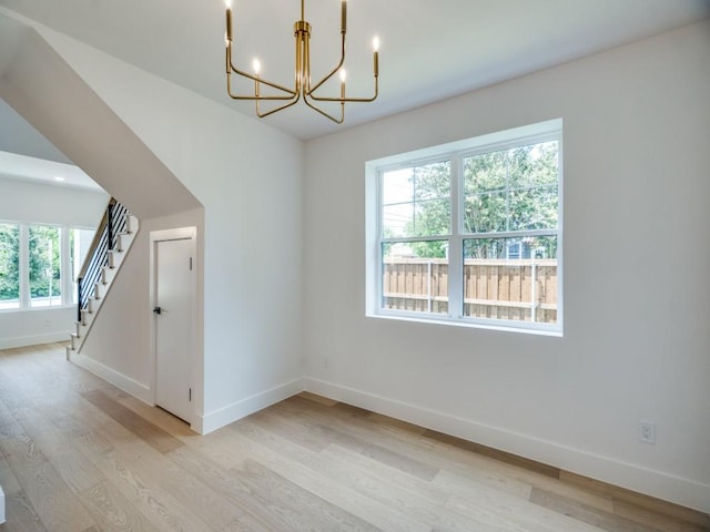 empty room with baseboards, stairs, light wood-style flooring, and a notable chandelier