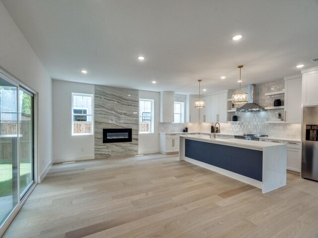 kitchen with decorative backsplash, wall chimney exhaust hood, a sink, open shelves, and stainless steel fridge with ice dispenser