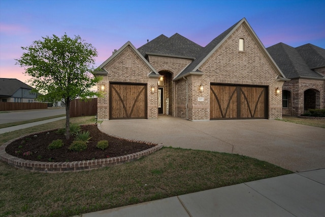 french country home featuring fence, concrete driveway, brick siding, and a garage