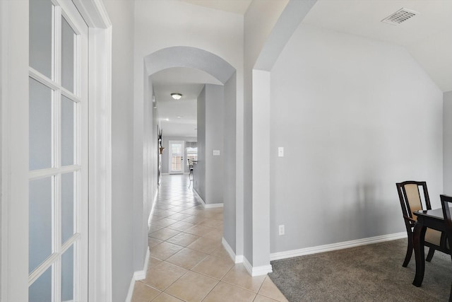hallway featuring arched walkways, visible vents, baseboards, and light tile patterned floors