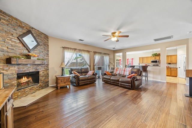 living room with ceiling fan, a stone fireplace, light wood-style floors, and visible vents