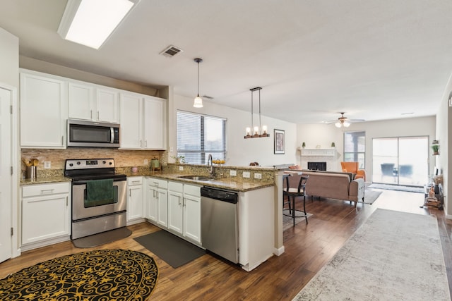 kitchen with a sink, a fireplace, a peninsula, stainless steel appliances, and visible vents
