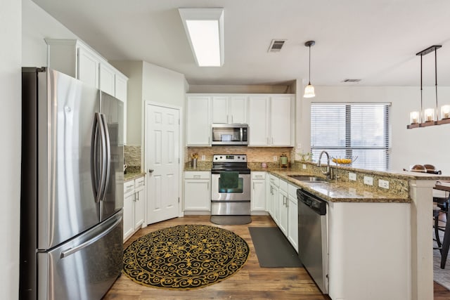 kitchen featuring visible vents, a peninsula, wood finished floors, stainless steel appliances, and a sink