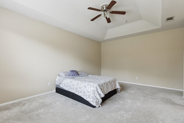 carpeted bedroom with a tray ceiling, baseboards, visible vents, and ceiling fan