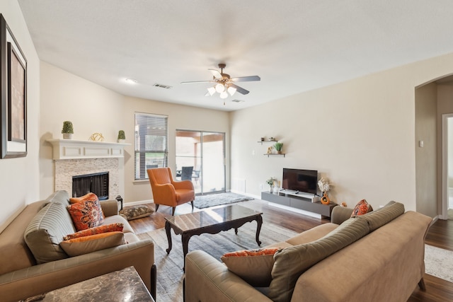living area featuring arched walkways, visible vents, a ceiling fan, a tile fireplace, and wood finished floors