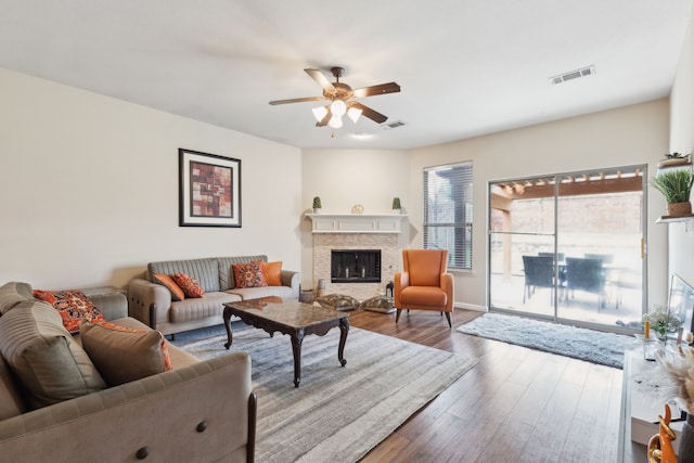 living room with visible vents, wood finished floors, a fireplace, and a ceiling fan