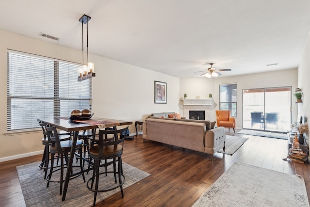dining space featuring ceiling fan with notable chandelier, dark wood-type flooring, a fireplace, and visible vents