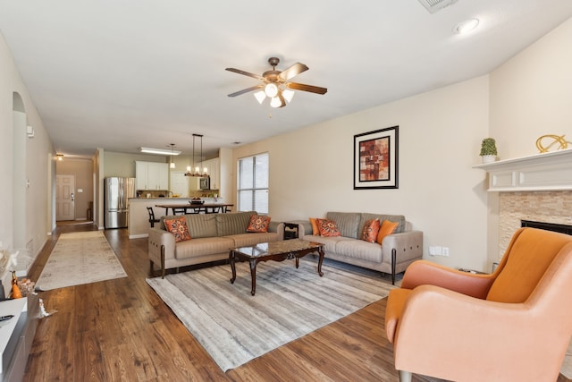 living area with ceiling fan with notable chandelier, a fireplace, and dark wood-style floors