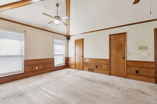 unfurnished room with a ceiling fan, wainscoting, a textured ceiling, wooden walls, and lofted ceiling
