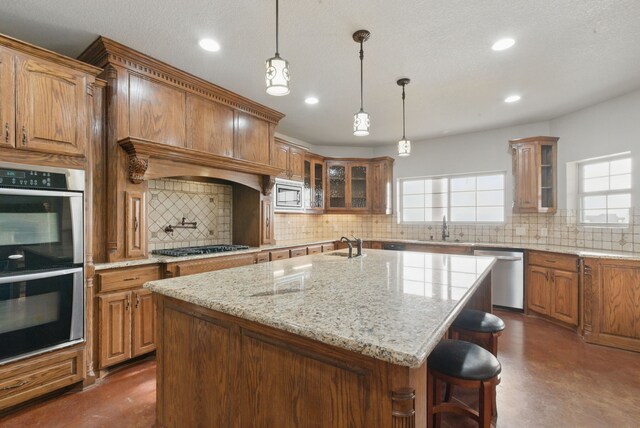 kitchen featuring stainless steel appliances, glass insert cabinets, a sink, an island with sink, and a kitchen breakfast bar