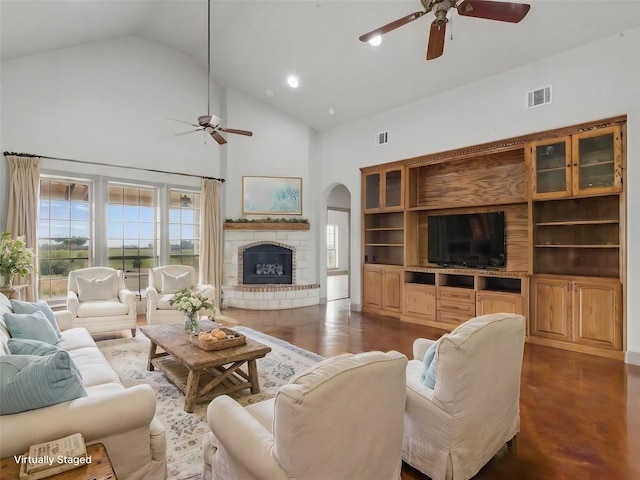 living area featuring a fireplace with raised hearth, visible vents, arched walkways, and ceiling fan