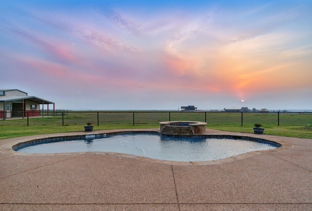 pool at dusk featuring a patio area, a pool with connected hot tub, fence, and a yard