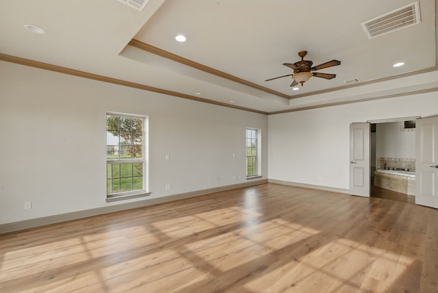 spare room with light wood finished floors, visible vents, ceiling fan, and a raised ceiling