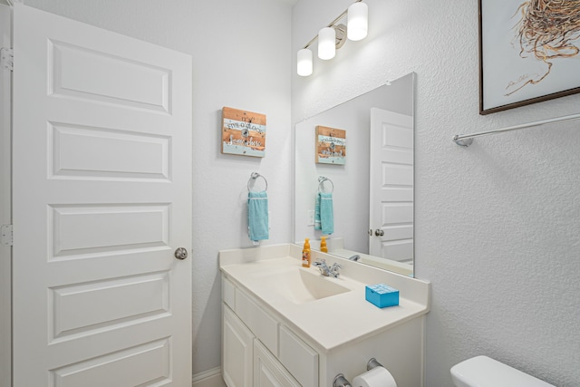 bathroom featuring vanity, a textured wall, and toilet