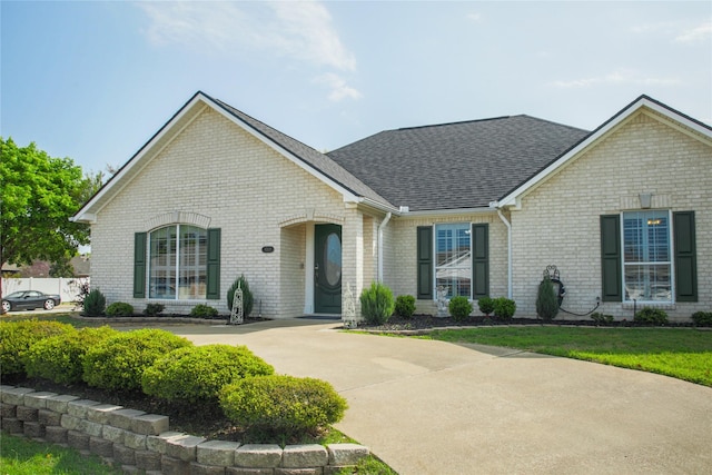 view of front of property with brick siding, a shingled roof, a front lawn, and fence