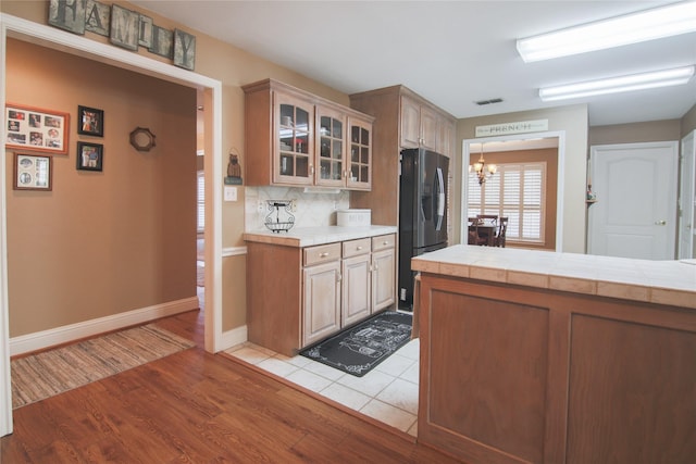 kitchen with visible vents, glass insert cabinets, light wood-type flooring, stainless steel fridge with ice dispenser, and an inviting chandelier