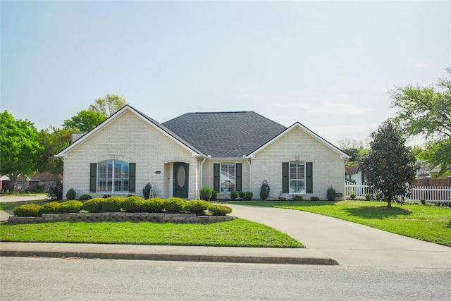 view of front of house featuring brick siding, a front yard, curved driveway, and fence