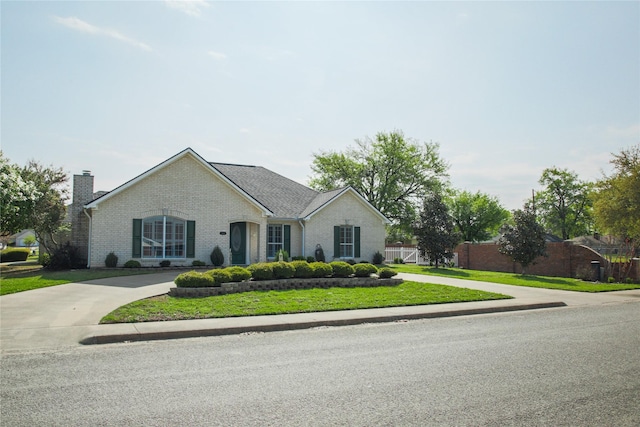 view of front of house with brick siding, a chimney, curved driveway, and fence