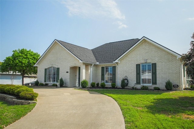 view of front of house with brick siding, a front yard, driveway, and a shingled roof
