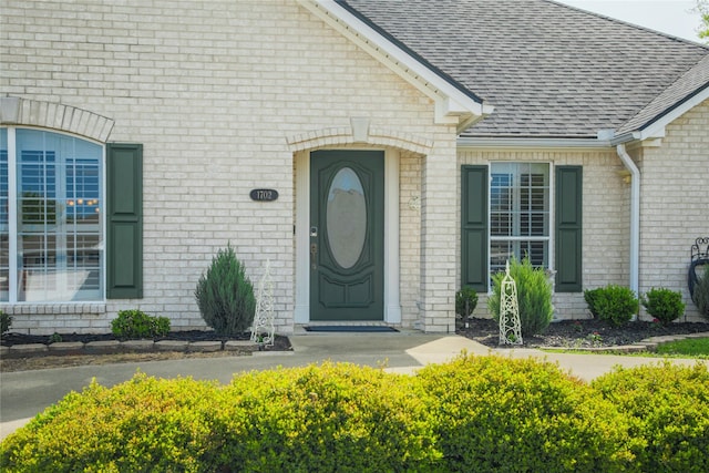 doorway to property with brick siding and a shingled roof