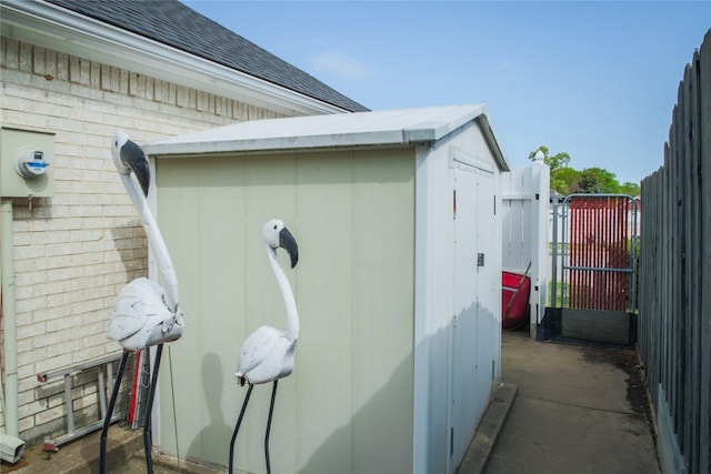 view of side of property with an outdoor structure, fence, a gate, brick siding, and a storage shed