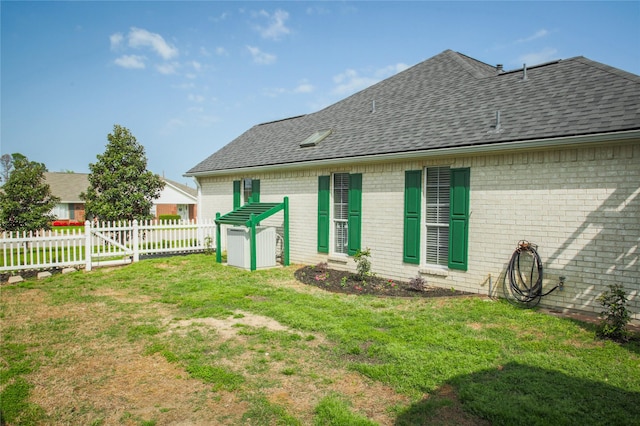 back of house with a lawn, brick siding, fence, and roof with shingles