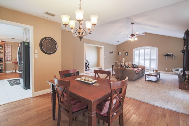 dining room featuring visible vents, light wood-style flooring, vaulted ceiling, and ceiling fan with notable chandelier