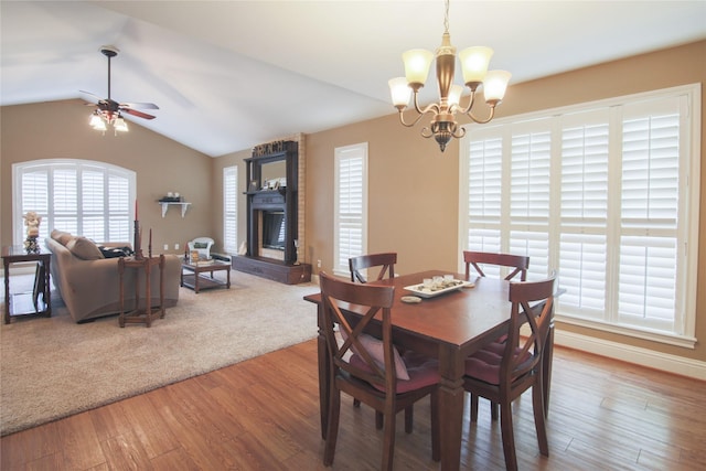 dining space with lofted ceiling, ceiling fan with notable chandelier, baseboards, a fireplace, and wood finished floors