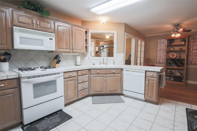 kitchen featuring a ceiling fan, a sink, tile counters, and white appliances