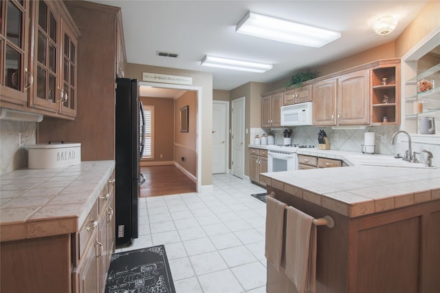 kitchen with white appliances, light tile patterned floors, decorative backsplash, a sink, and glass insert cabinets