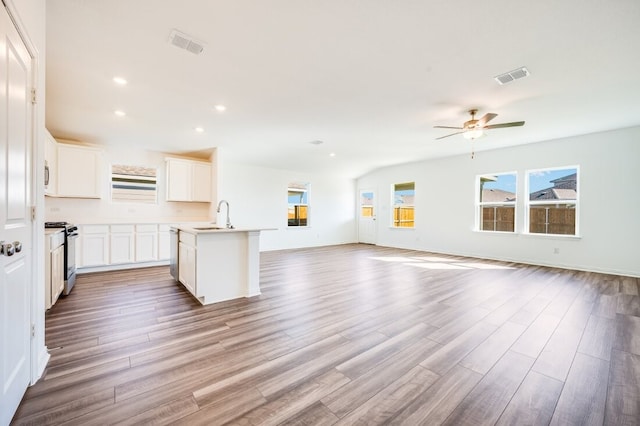 kitchen with a center island with sink, open floor plan, light wood-type flooring, gas range oven, and visible vents