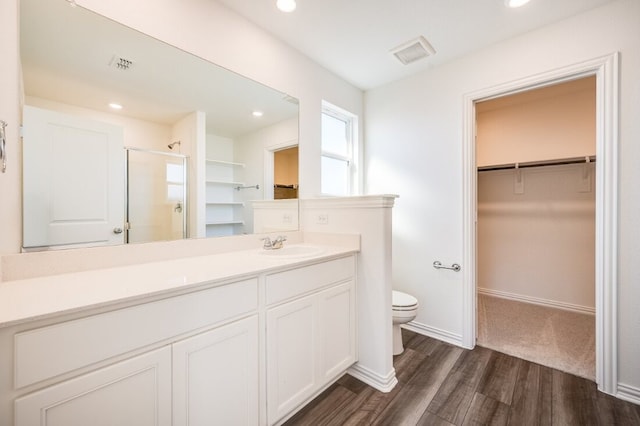 bathroom featuring a spacious closet, toilet, a shower stall, visible vents, and wood finished floors