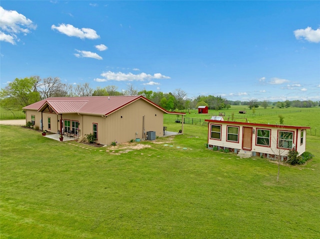 back of property featuring central AC, a patio area, a rural view, and a yard