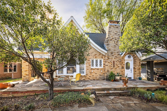view of front of house featuring brick siding, a shingled roof, a chimney, and a patio area