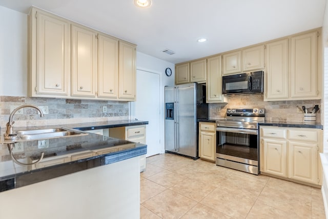kitchen with cream cabinets, a sink, stainless steel appliances, and dark countertops