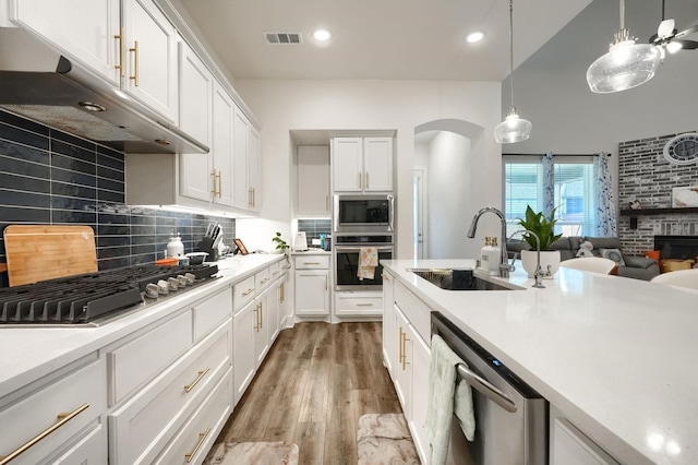 kitchen with a sink, appliances with stainless steel finishes, under cabinet range hood, visible vents, and arched walkways
