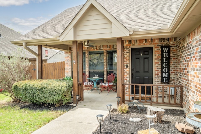 doorway to property featuring brick siding, a shingled roof, fence, and a porch