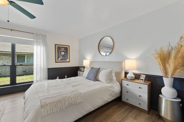bedroom featuring wainscoting, wood finished floors, and ceiling fan