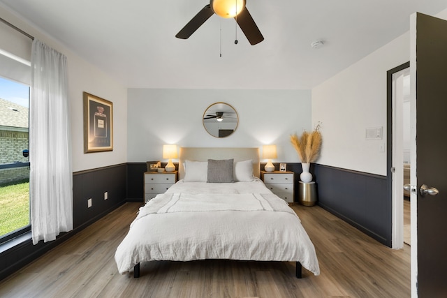 bedroom featuring a wainscoted wall, wood finished floors, and a ceiling fan