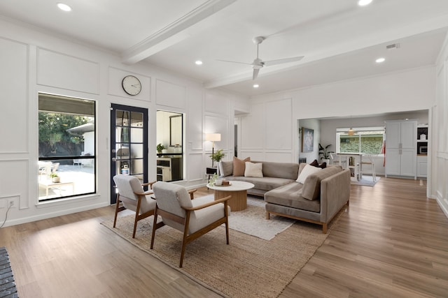 living area with a decorative wall, light wood finished floors, and beam ceiling