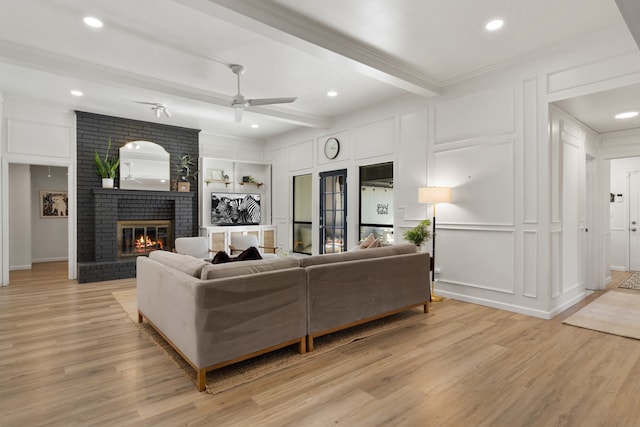 living area featuring a decorative wall, a brick fireplace, beamed ceiling, and light wood-style flooring
