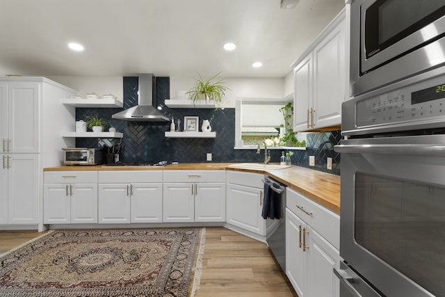 kitchen featuring wood counters, stainless steel appliances, wall chimney exhaust hood, a sink, and open shelves