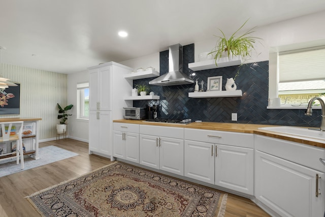 kitchen featuring wall chimney range hood, butcher block counters, a sink, and open shelves