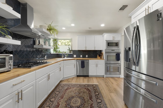 kitchen featuring wood counters, wall chimney exhaust hood, appliances with stainless steel finishes, and open shelves