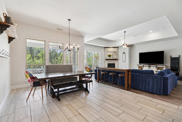 2602 Cypress Dr, Rockwall, TX 75087 - dining room with wood tiled floor, a stone fireplace, baseboards, ceiling fan with notable chandelier, and a tray ceiling